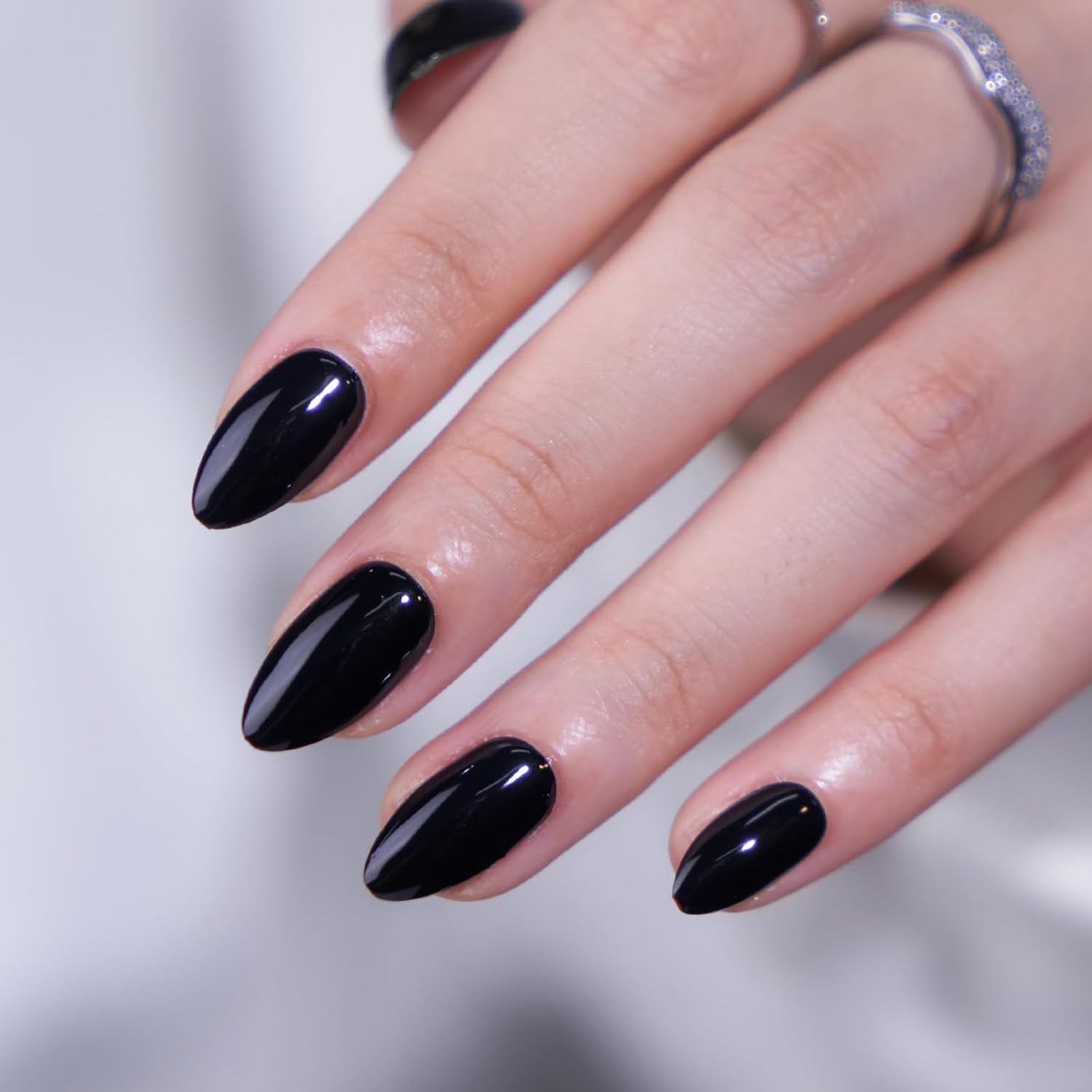 Hand wearing short almond black press-on nails glossy gel finish